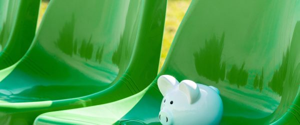 Piggy bank on the green chairs of sports stadium. Sports and money.