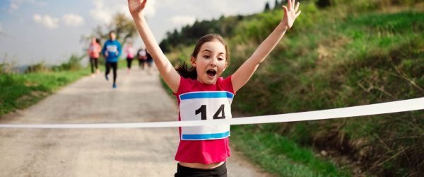 A small girl runner crossing finish line in a race competition in nature.